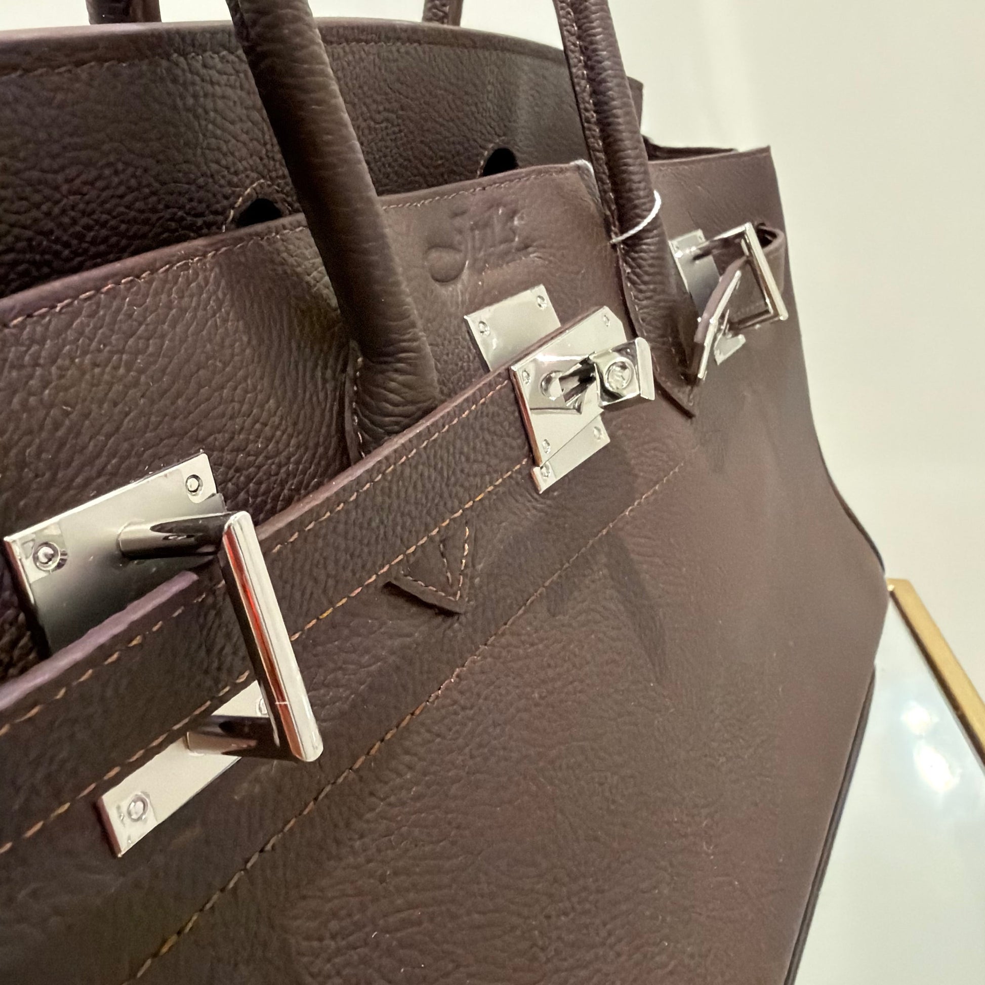 Close-up of a brown leather handbag with silver hardware on a light gray background