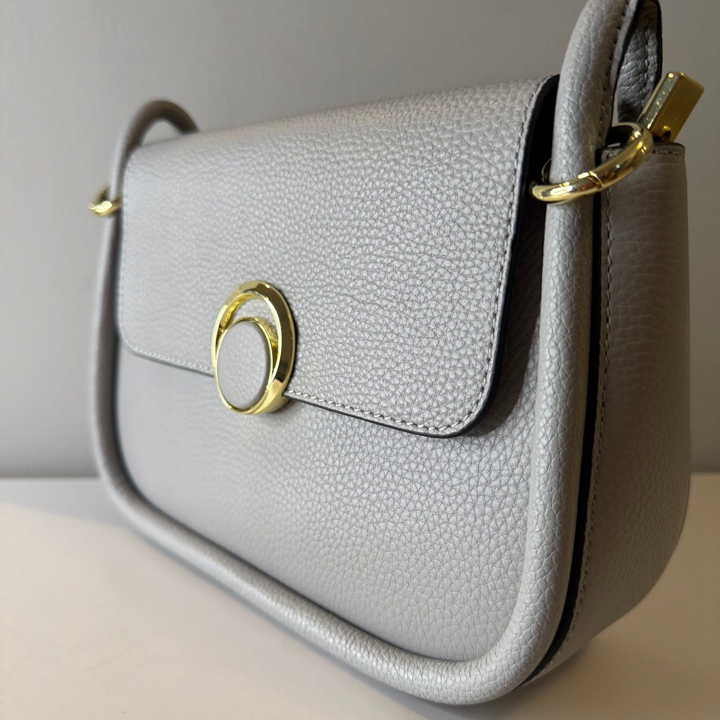Close-up of a gray handbag with gold accents on a neutral background