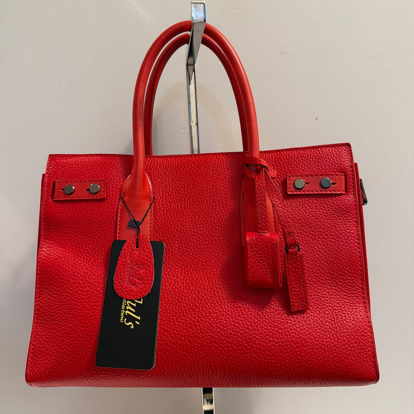 Red leather handbag with a tag on a light beige background