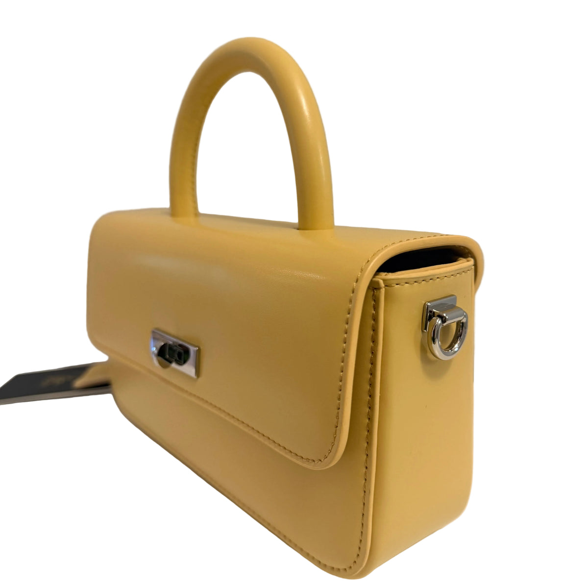 A small structured handbag in glossy mustard yellow leather with a top handle, silver-tone hardware, and a black-and-white tag, photographed on a light neutral surface against a plain light gray background.