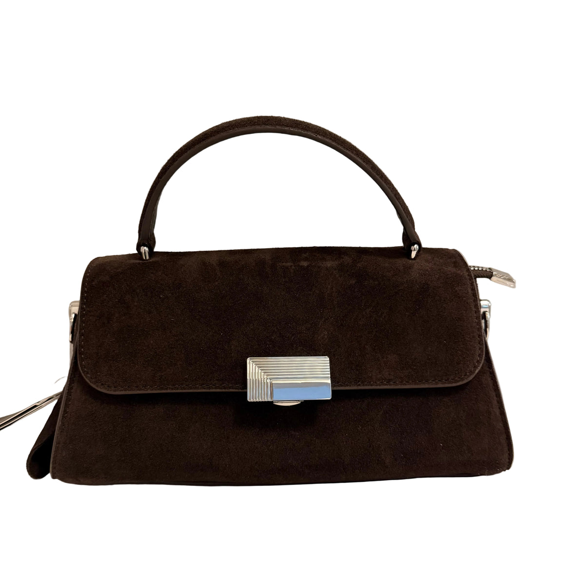 A dark brown suede handbag with a top handle and a silver-tone rectangular clasp, resting on a white surface against a light gray wall.