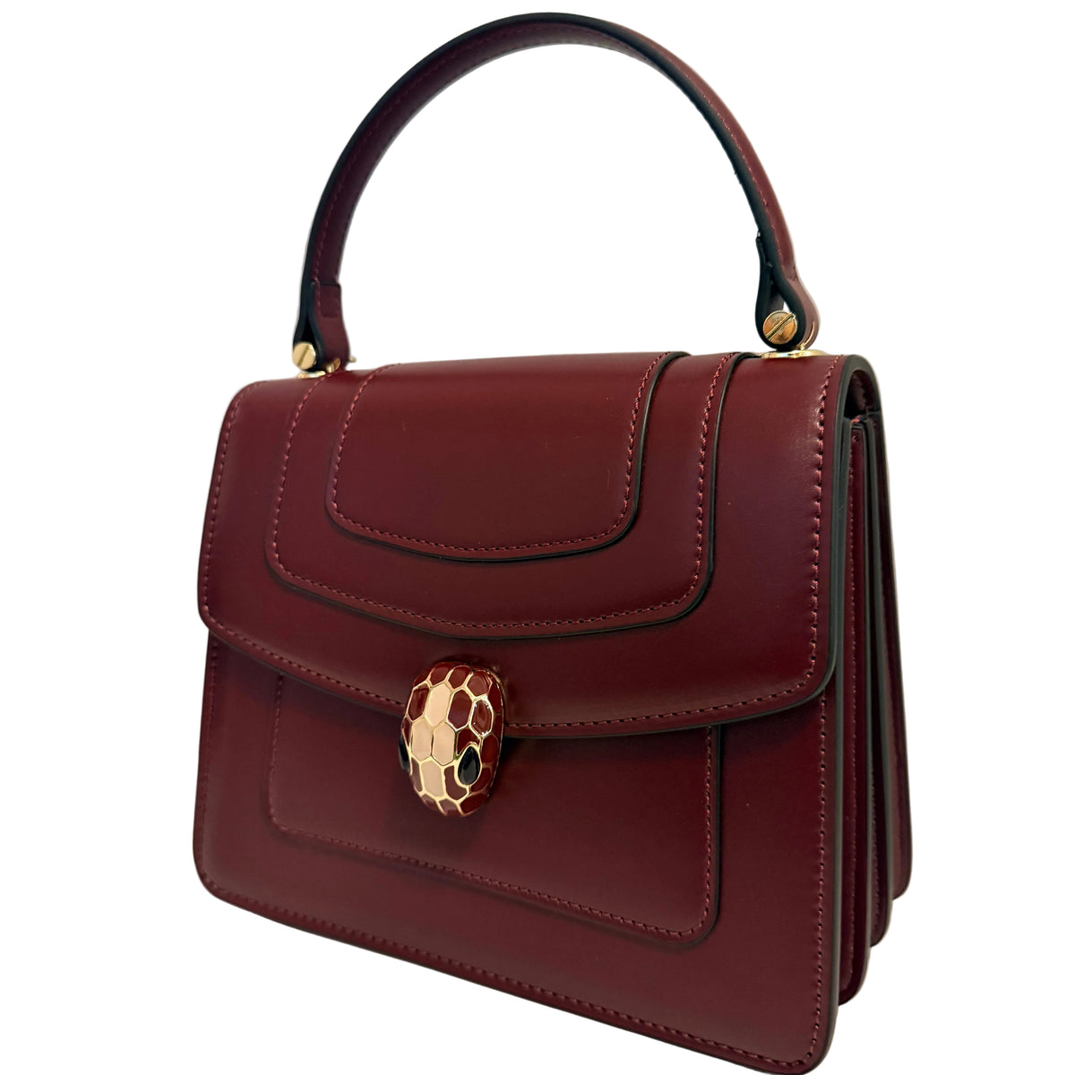 A dark burgundy leather handbag with a top handle and a gold-tone Serpenti snake clasp, shown against a plain off-white background.