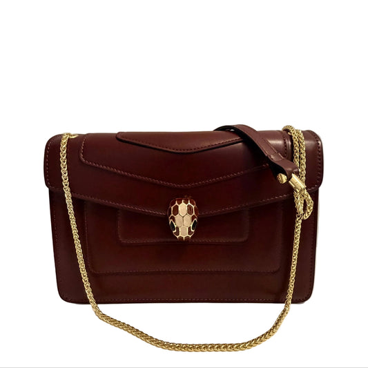 A dark burgundy leather shoulder bag with a gold chain strap and a metallic snake-head clasp, displayed on a white surface against a neutral gray background.