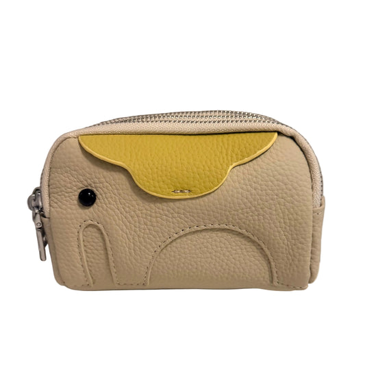 A small pebbled leather zip pouch in a light beige color with a contrasting yellow flap accent and a black stud detail, shown on a plain white surface against a gray wall.