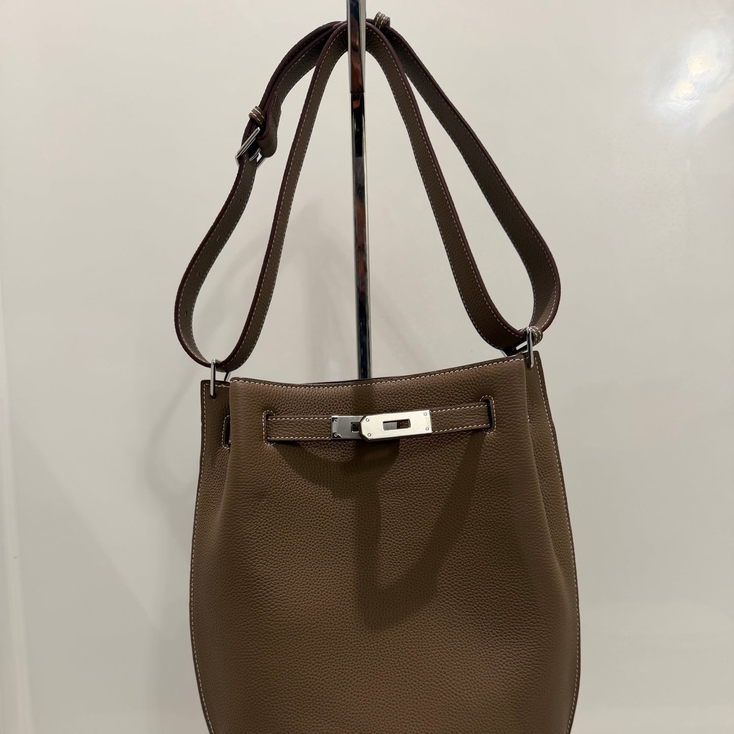 Brown leather handbag on a white surface with a mirror reflection.