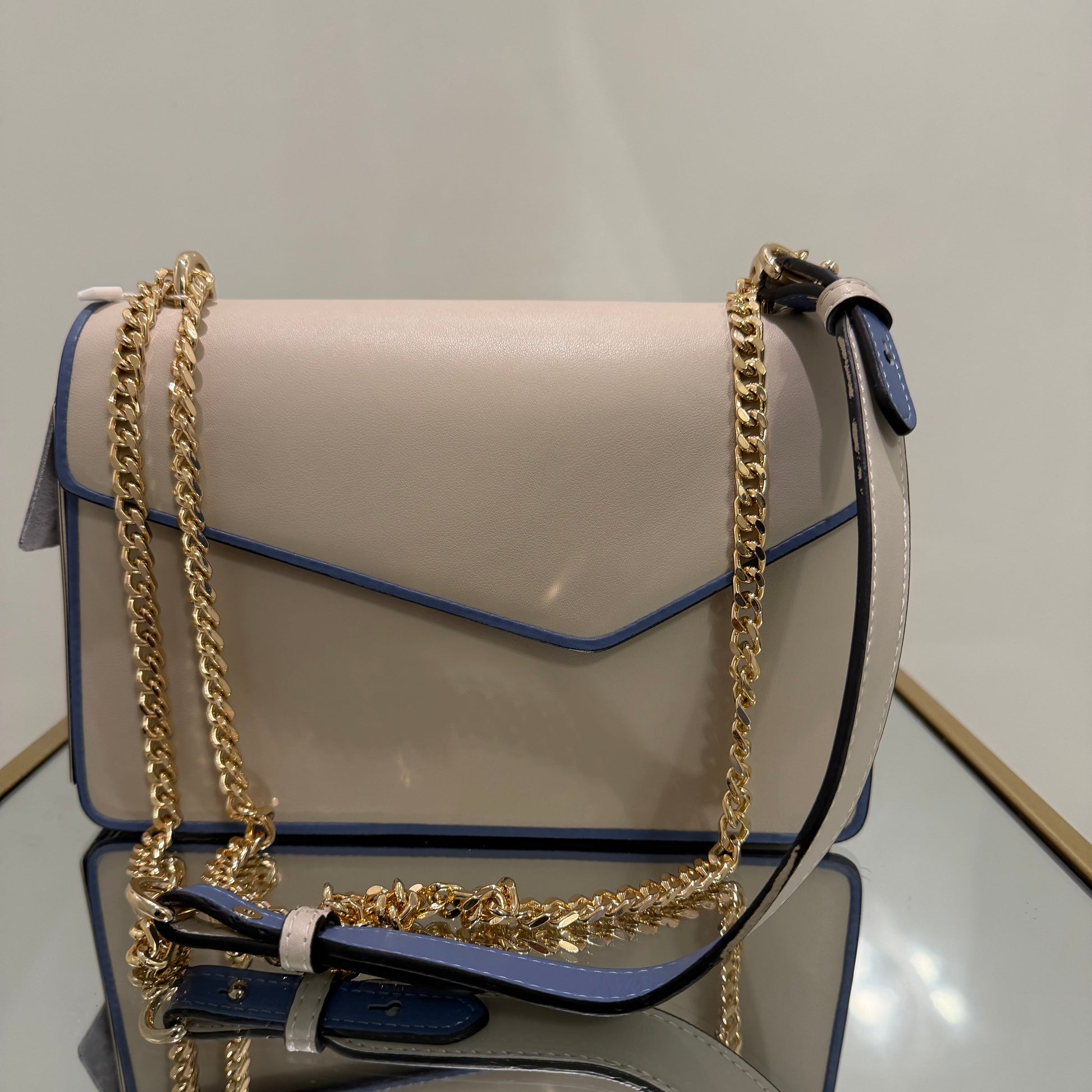 Beige handbag with gold chain strap on a mirror surface