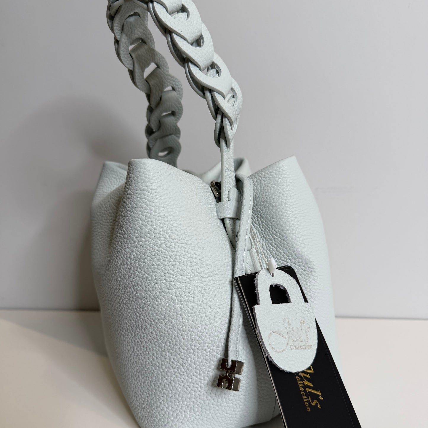 White leather handbag with braided handle on a light gray background