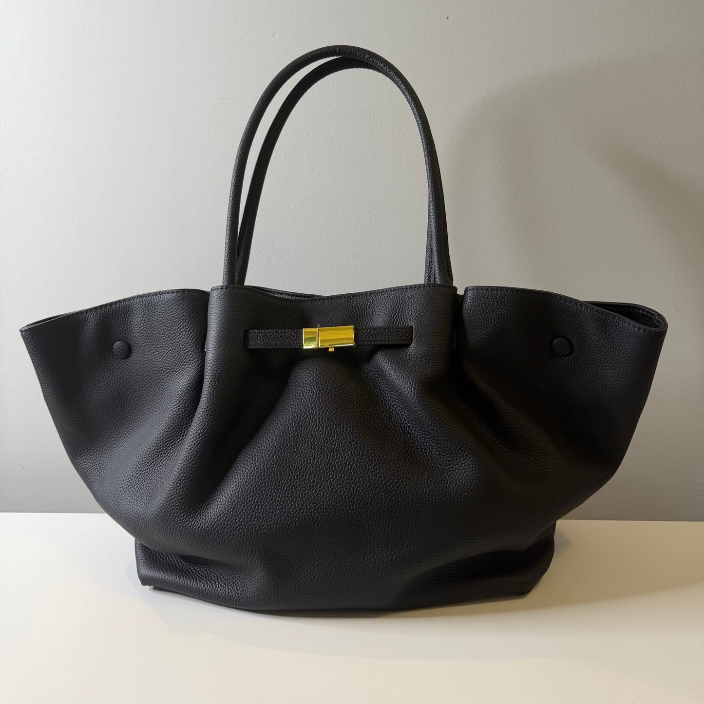 Black handbag with a gold clasp on a light gray background