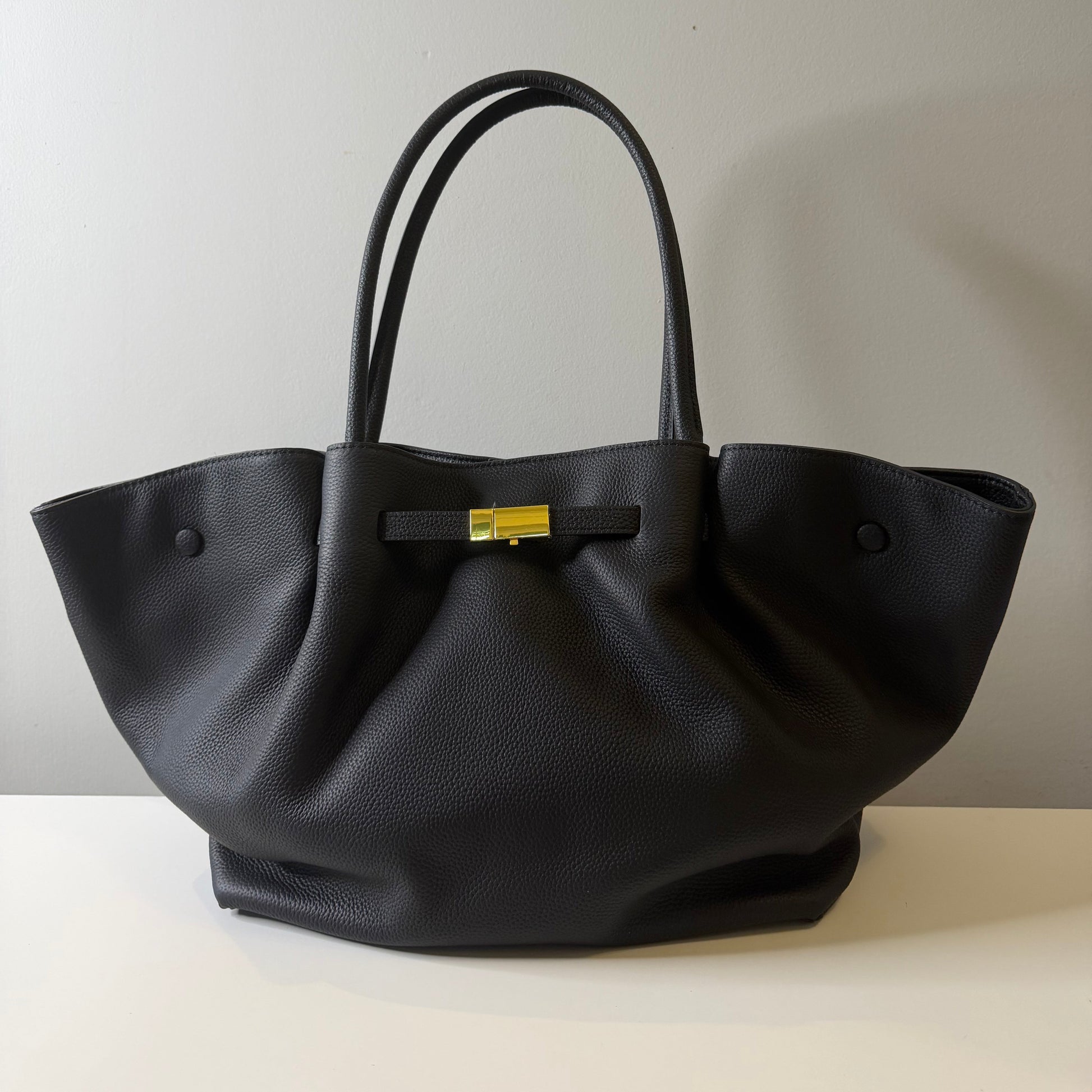 Black handbag with a gold clasp on a light gray background