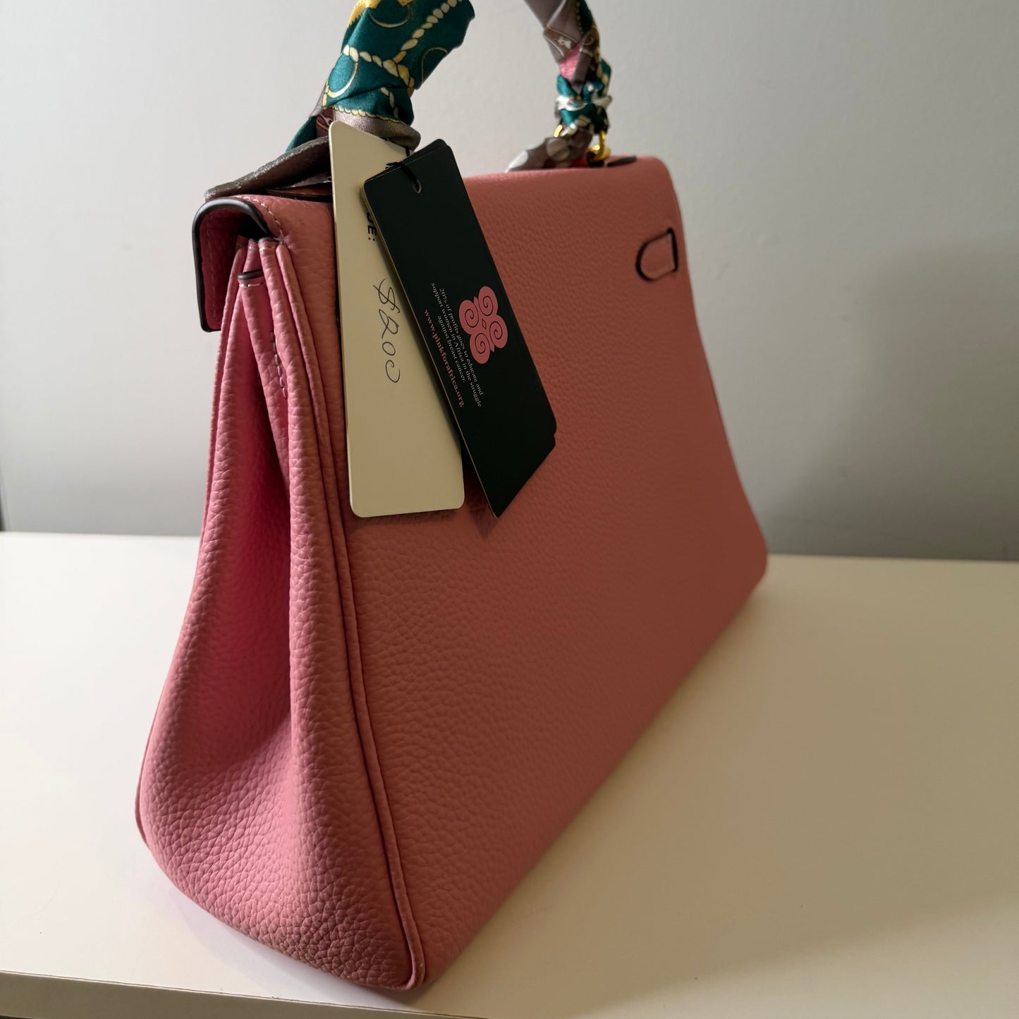 Pink handbag with floral strap and tags on a white background