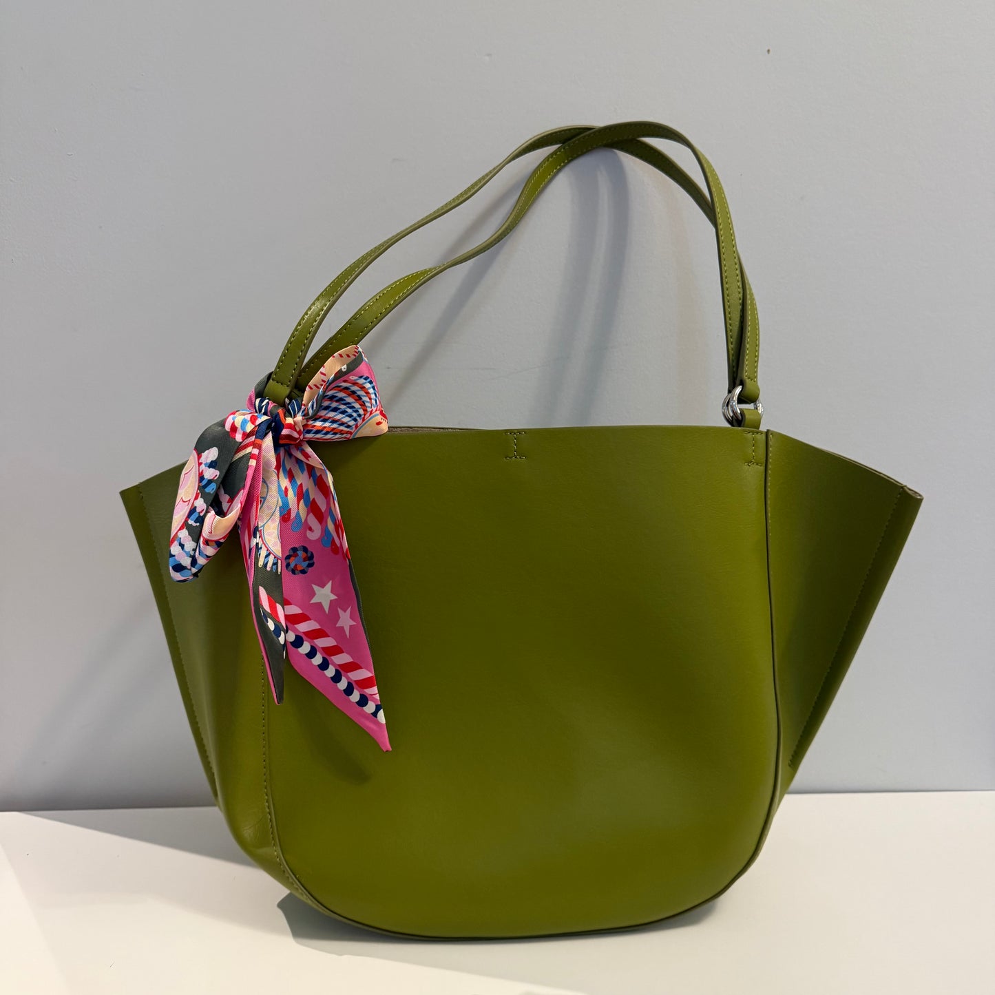 Green handbag with a colorful scarf on a gray background