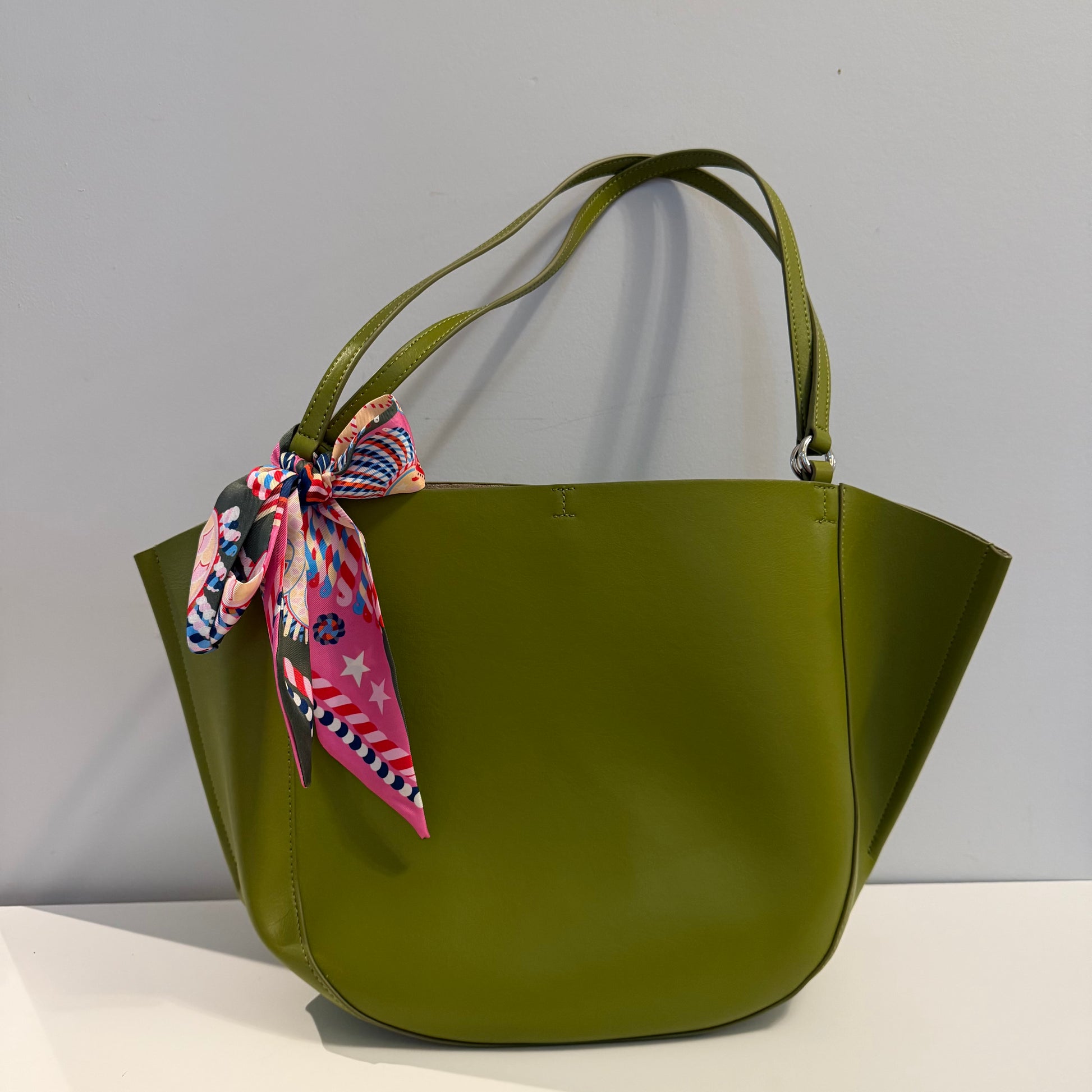 Green handbag with a colorful scarf tied around the handle on a gray background