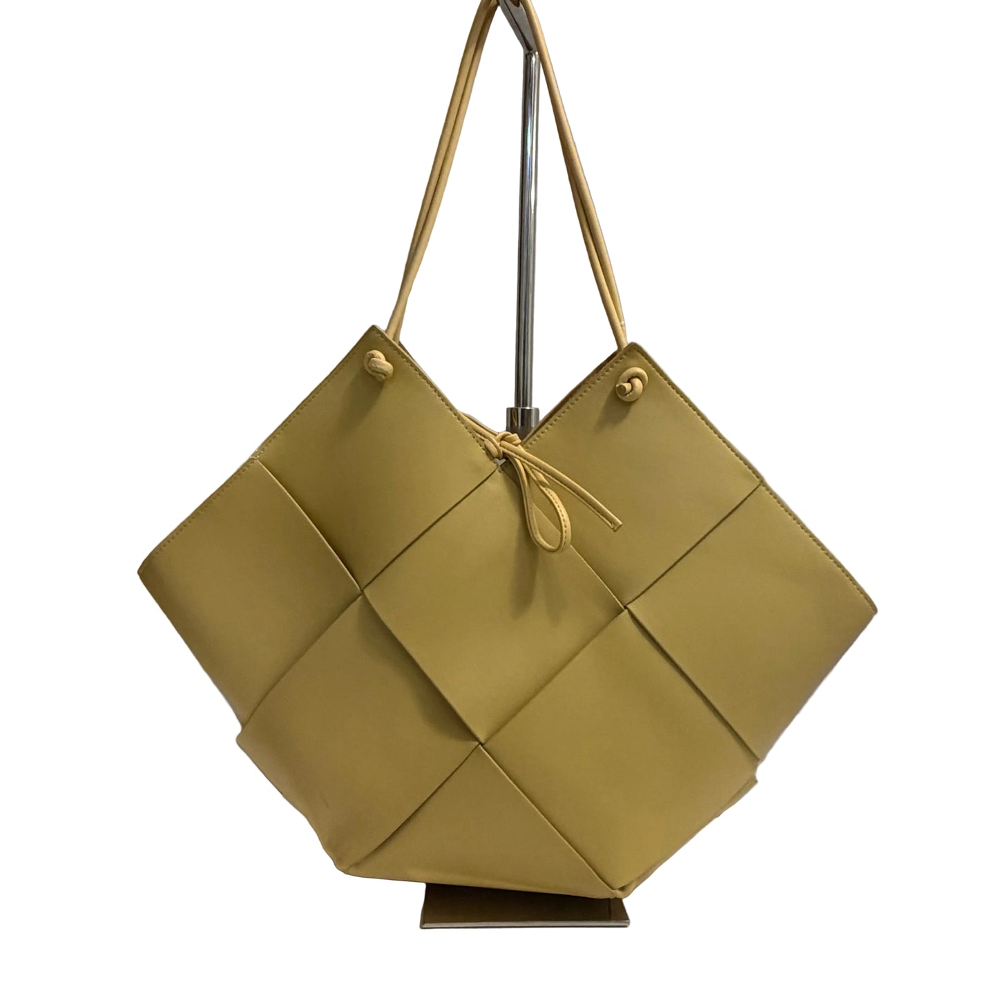 Green woven handbag on a stand against a gray background
