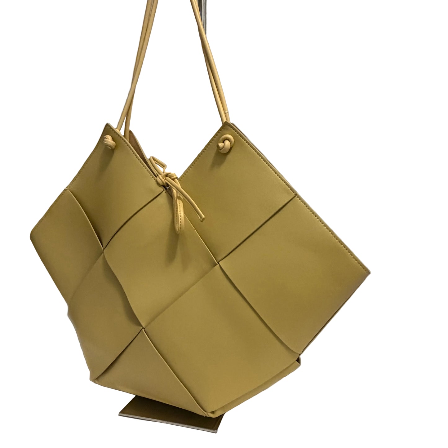 Green handbag with geometric design on a stand against a gray background