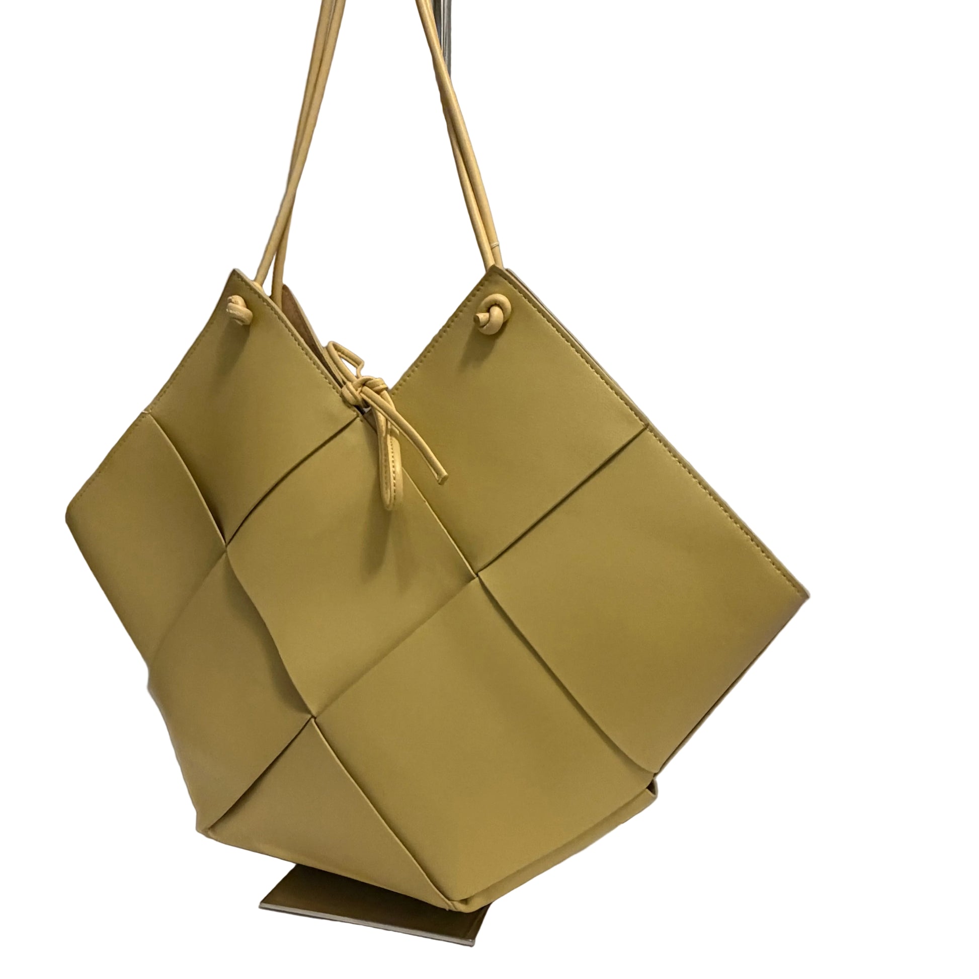 Green handbag with geometric design on a stand against a gray background
