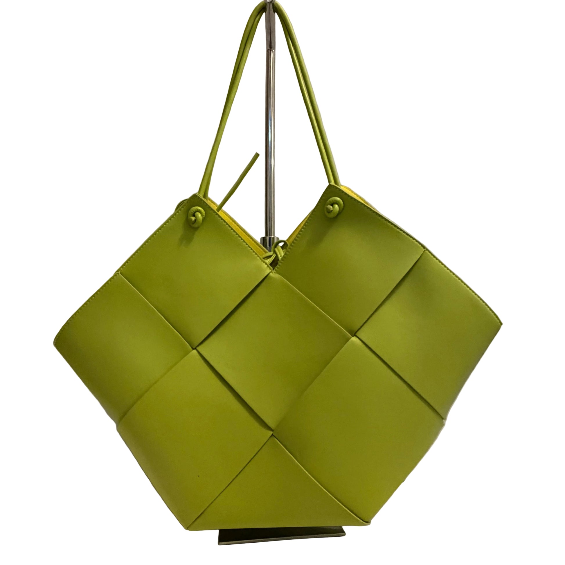 Green woven handbag on a white surface with a gray background