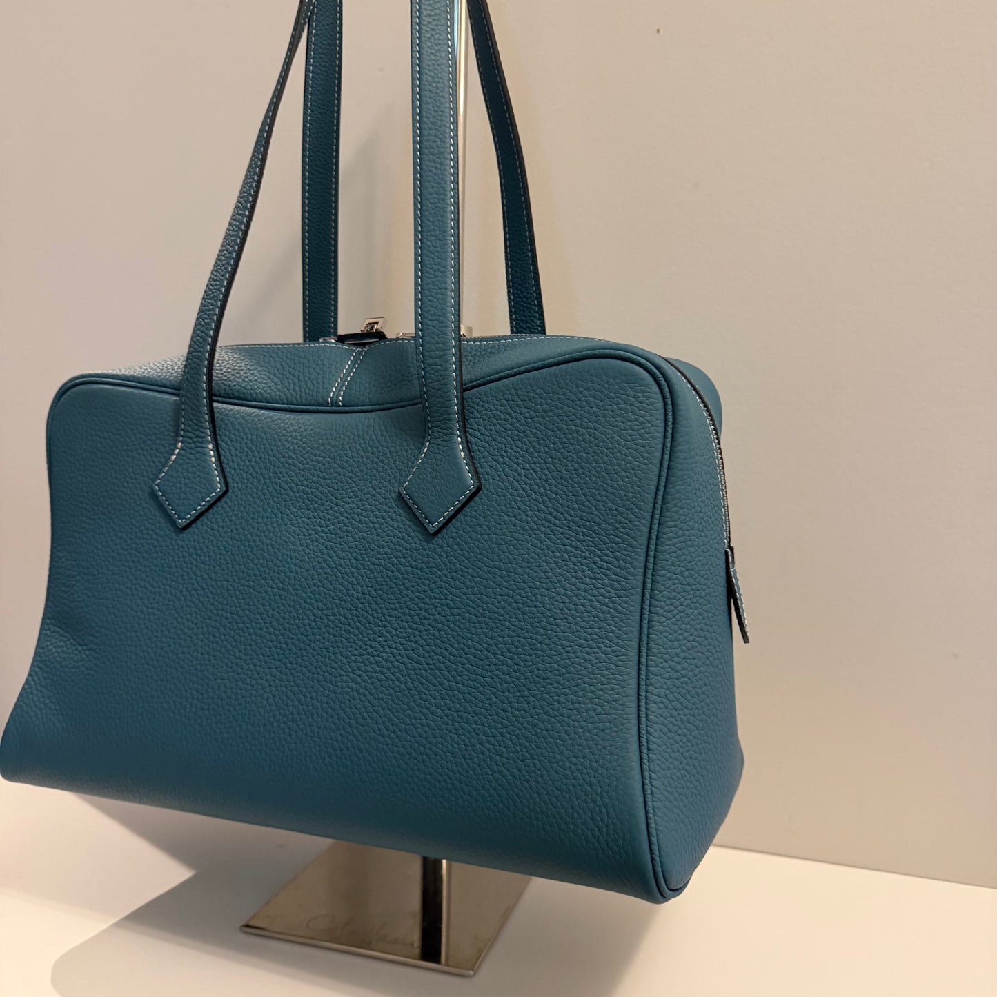 Blue handbag on a stand against a neutral background