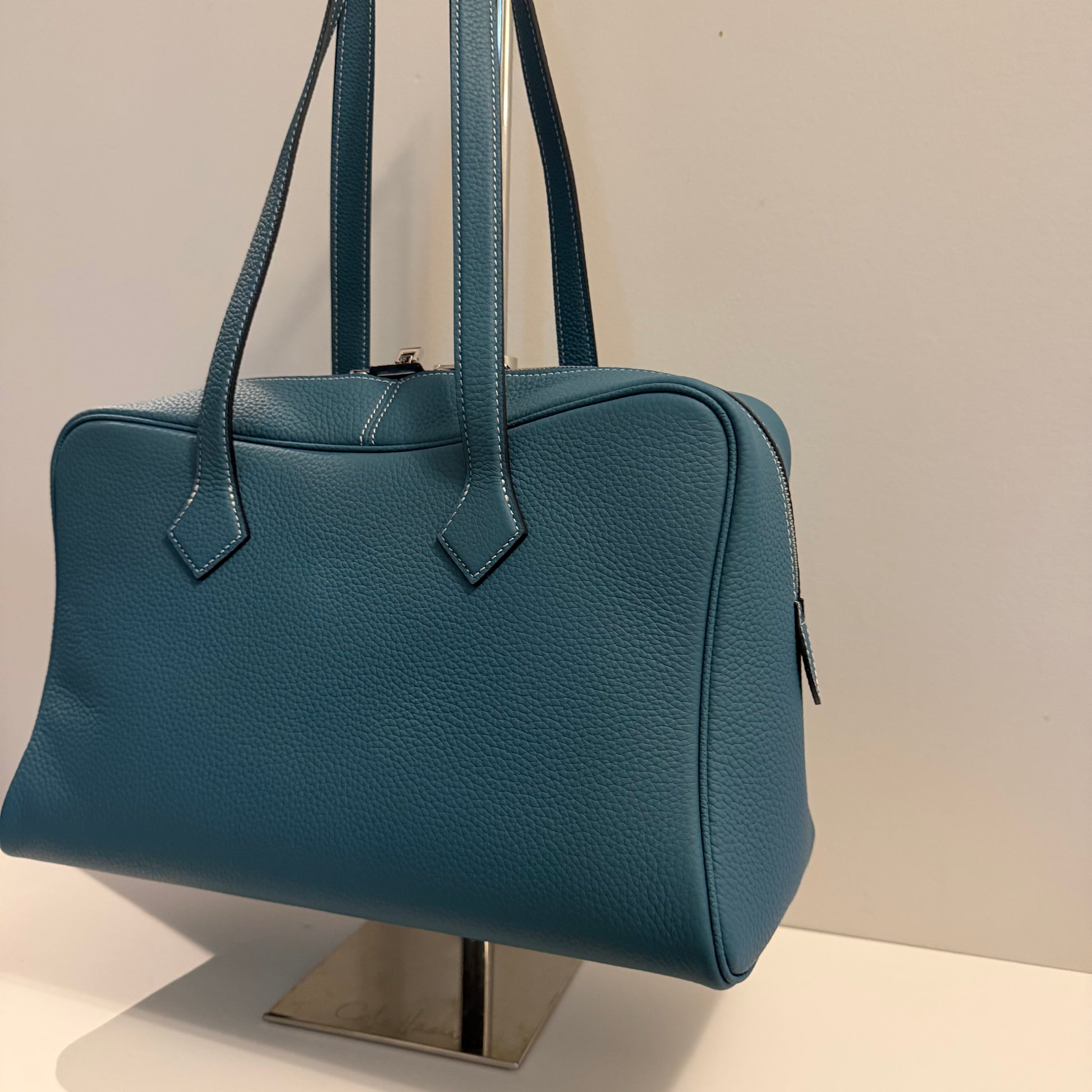 Blue handbag on a stand against a neutral background