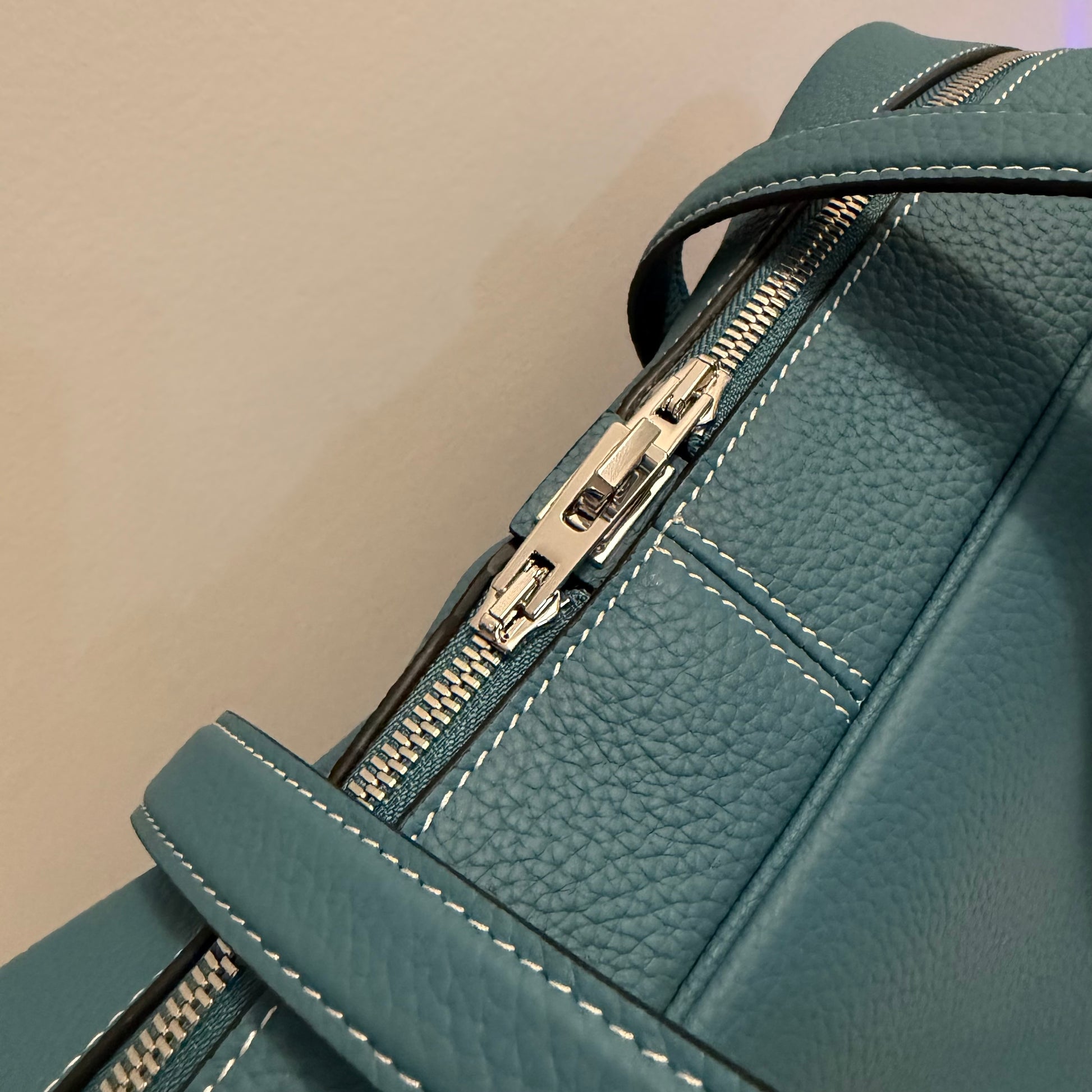 Teal leather backpack with gold zipper on a beige background