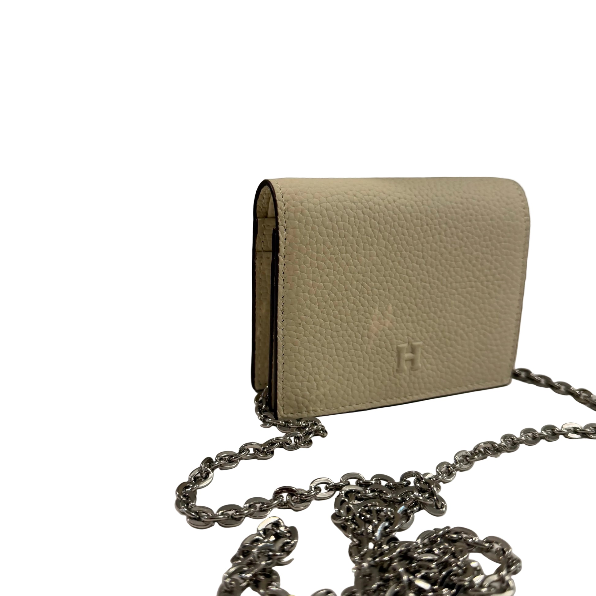 Beige handbag with a chain strap on a white surface against a gray background