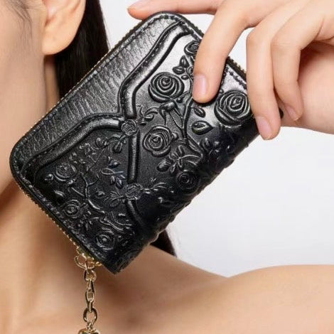Black embossed wallet with floral designs held by a person against a neutral background
