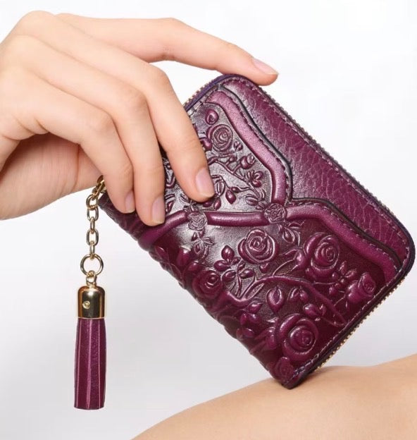 Purple wallet with floral embossing and tassel held by a hand on a white background