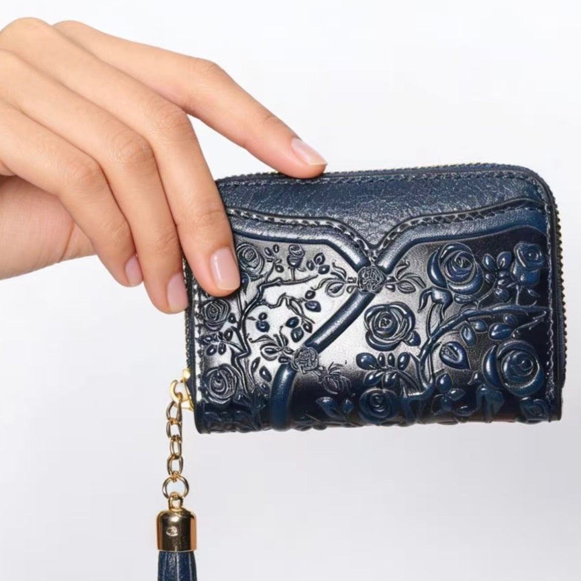 Hand holding a blue embroidered wallet with a tassel on a white background