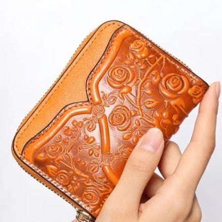 Hand holding an orange embossed wallet with a tassel on a light gray background