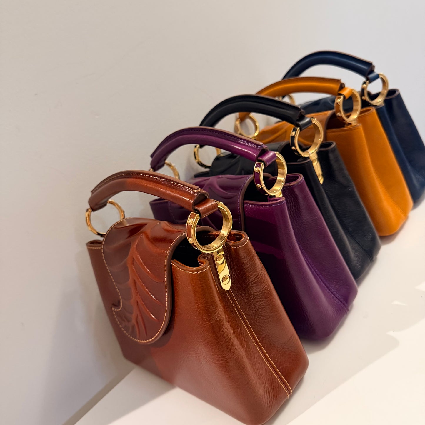 Row of handbags in various colors with gold handles on a light background