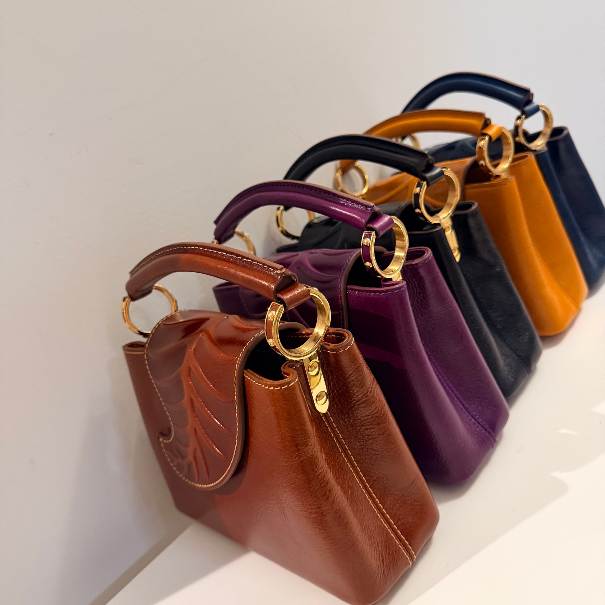 Row of handbags in various colors with gold handles on a light background