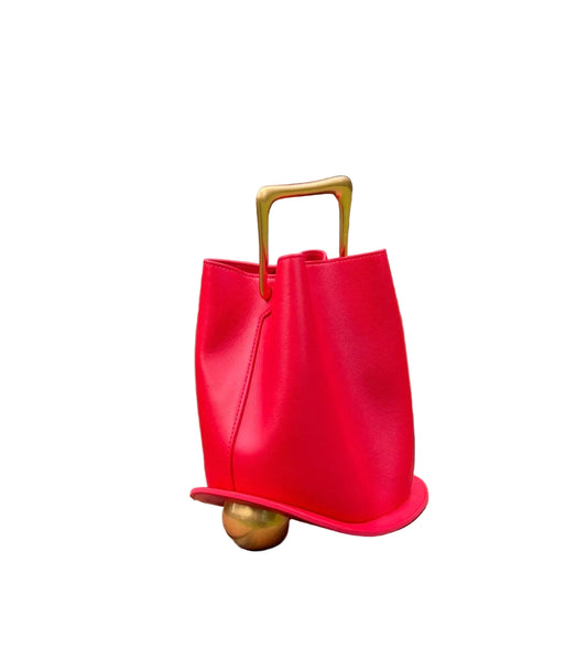 Red handbag with gold handle and base on a brick ledge in an outdoor setting