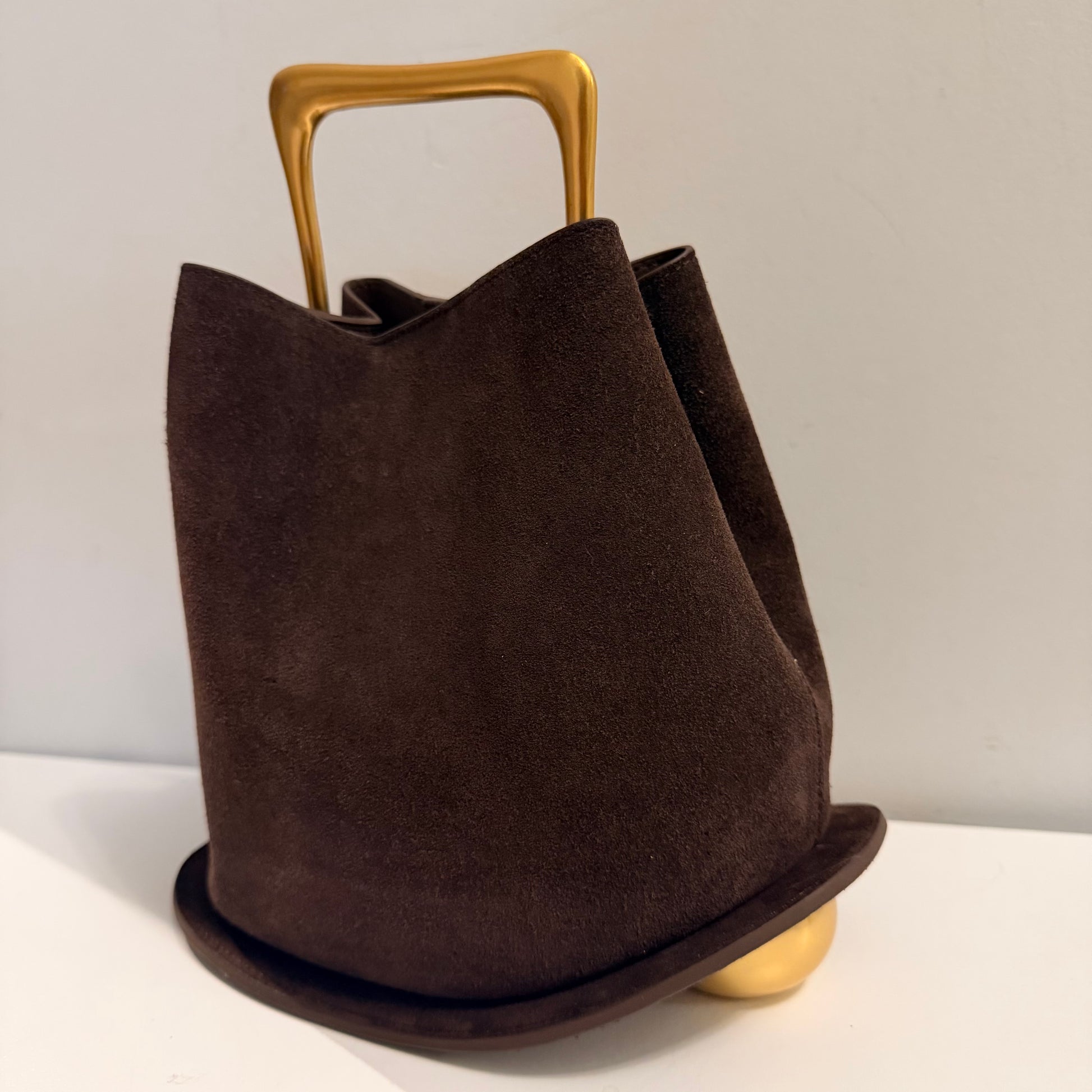 Brown suede handbag with gold handle and base on a light background