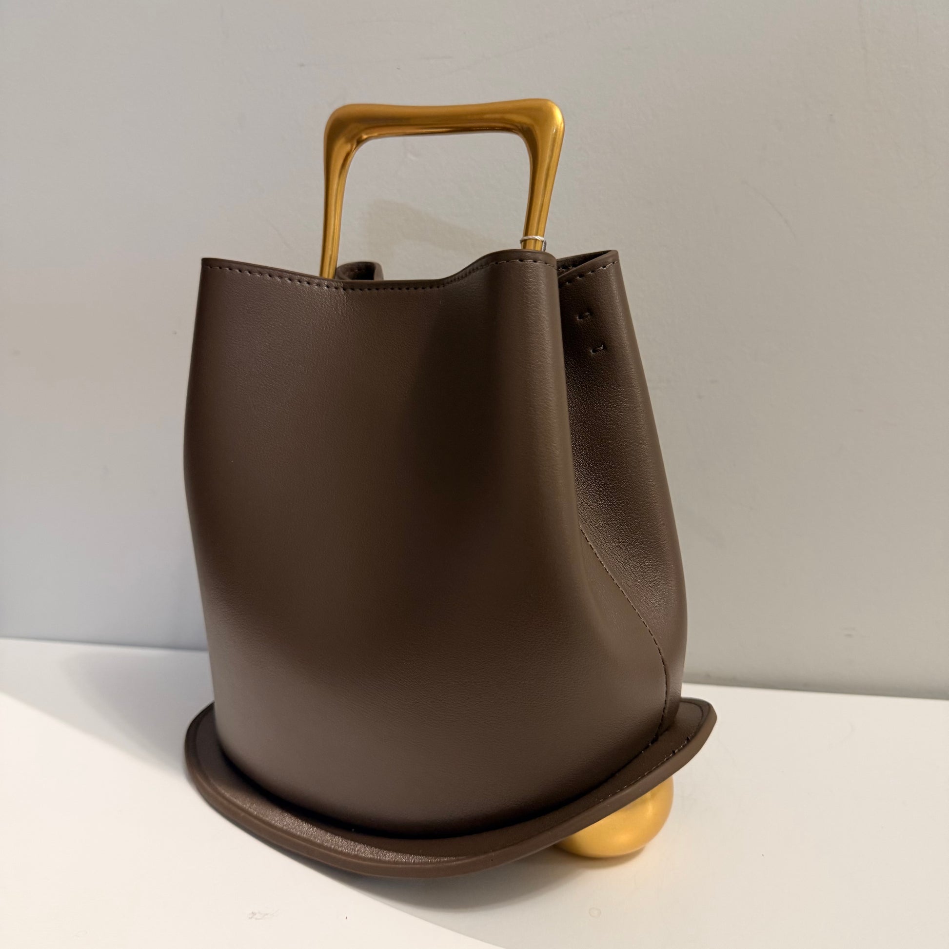 Brown leather bucket with gold accents on a light gray background
