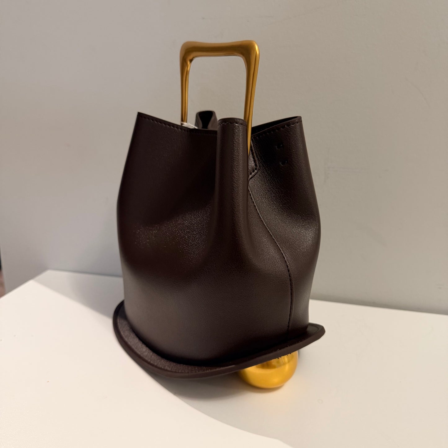 Brown leather handbag with a gold handle and base on a light surface.