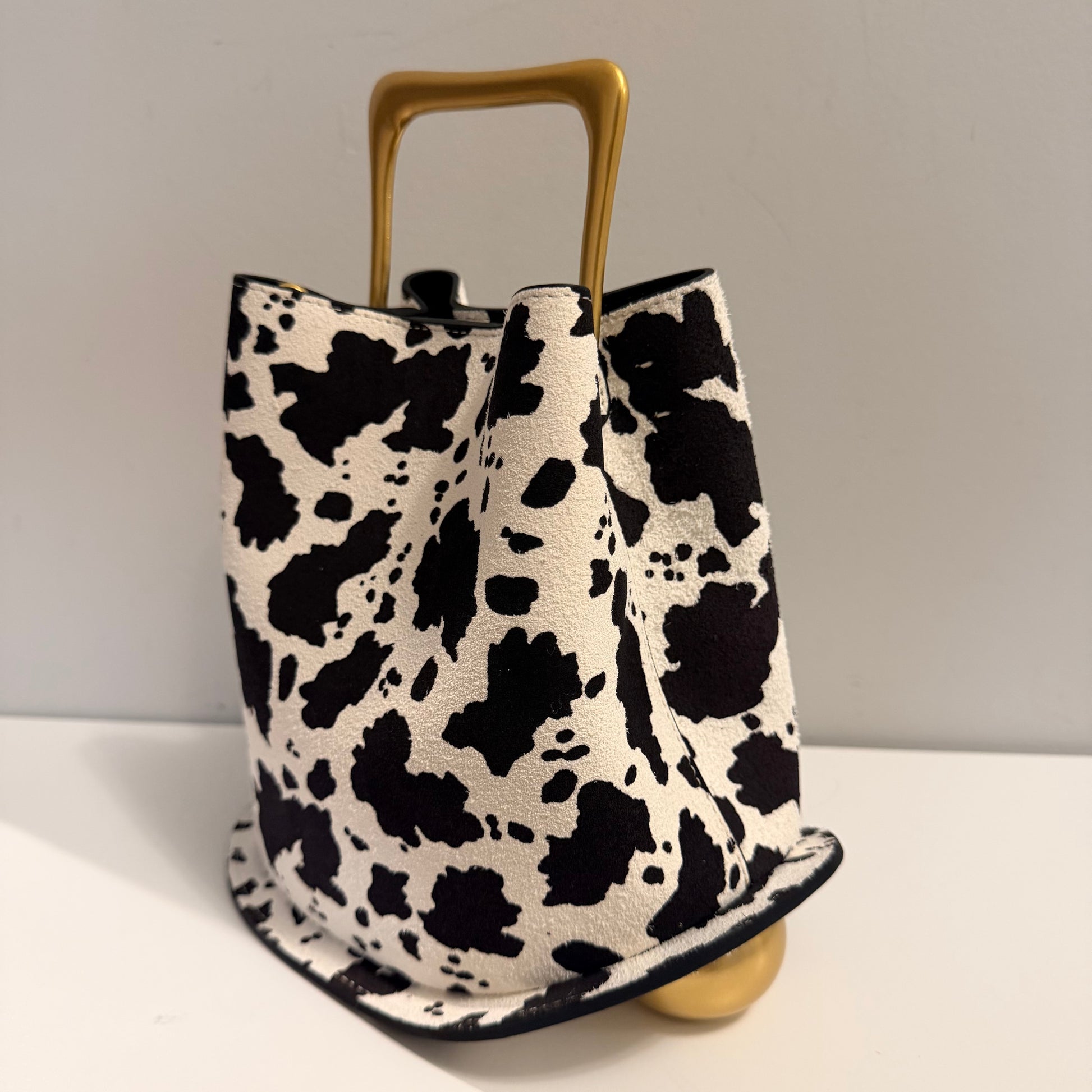 Black and white cow print bag with gold handle and base on a light gray background