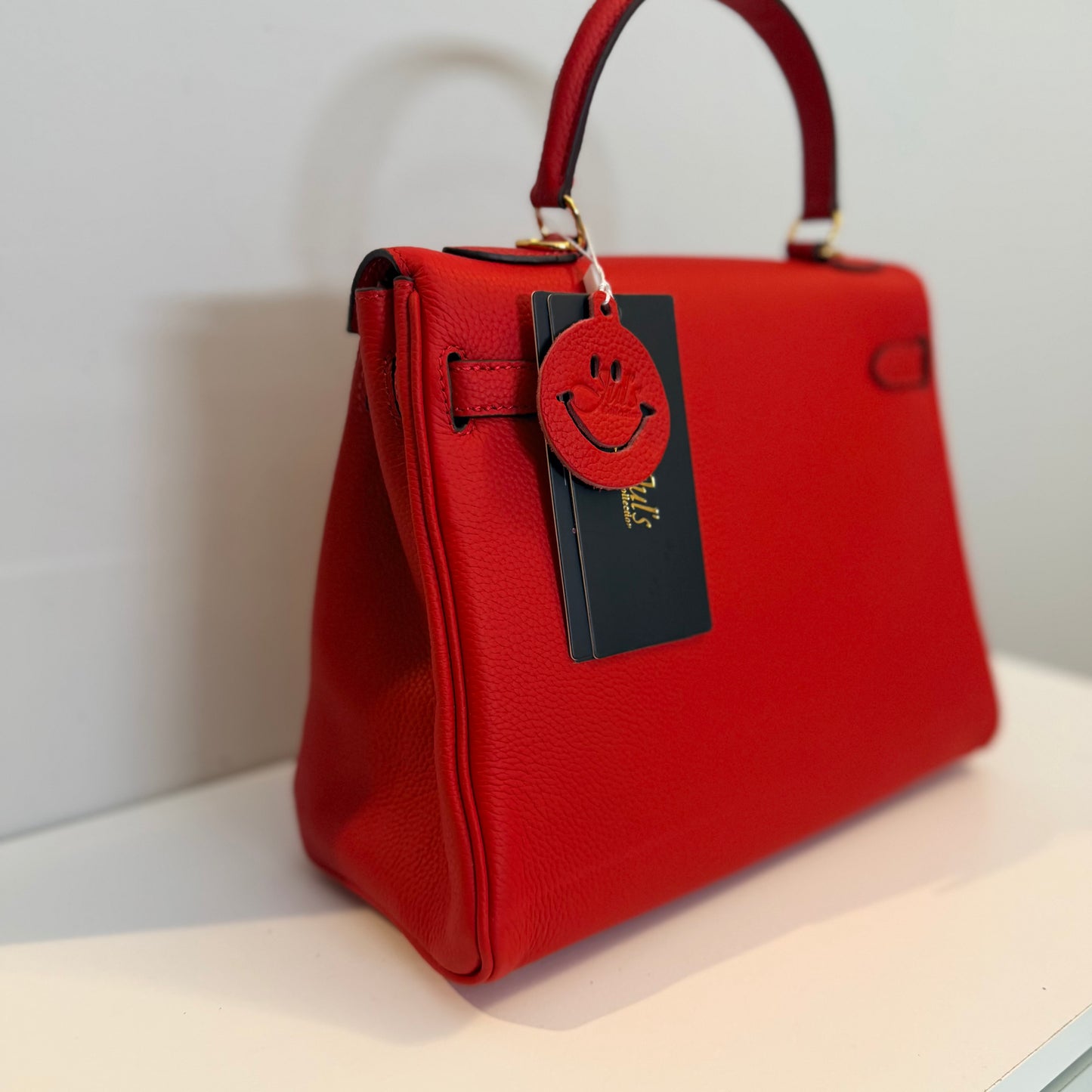 Red handbag with a smiley face tag on a light background