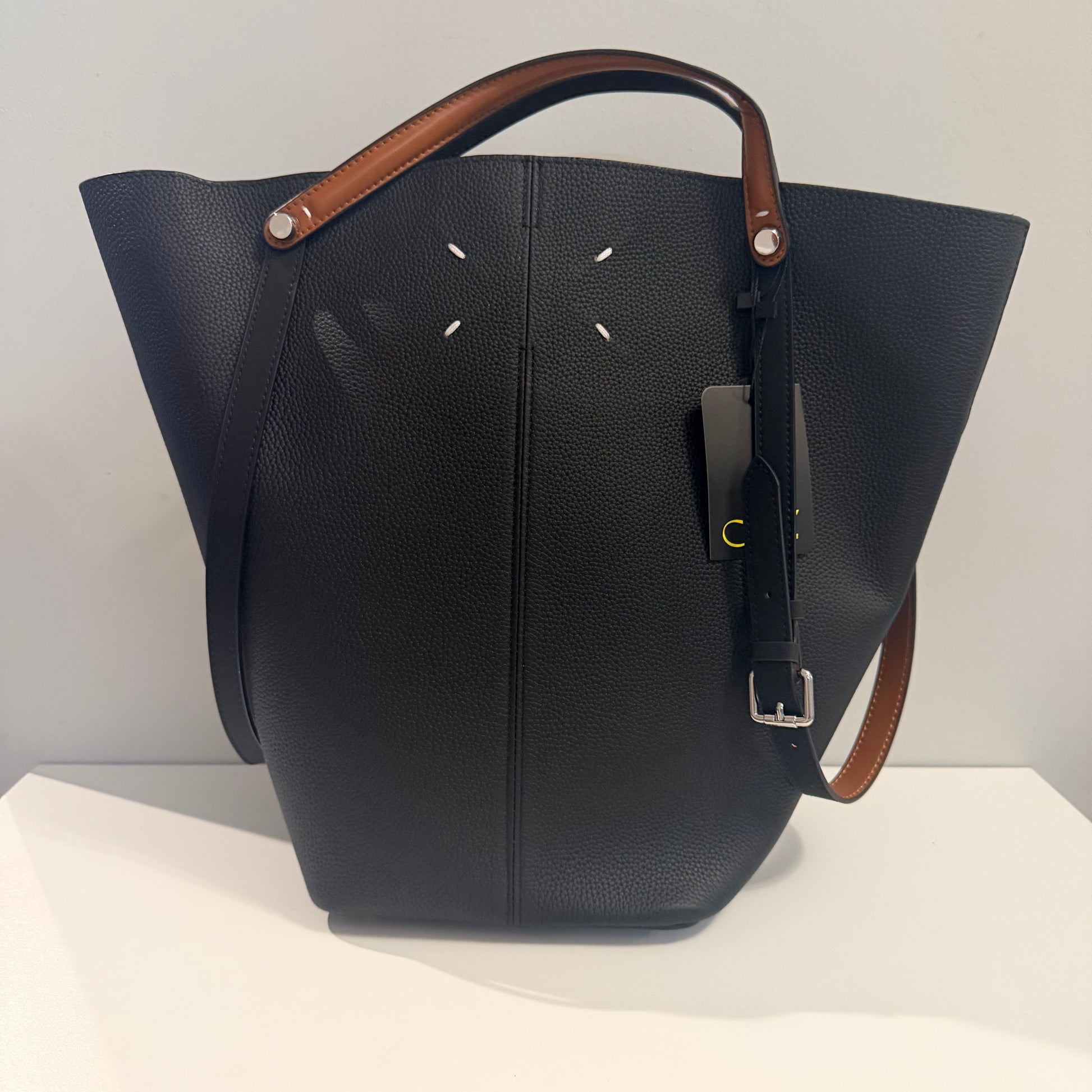 Black leather handbag with brown handle and strap on a white surface.