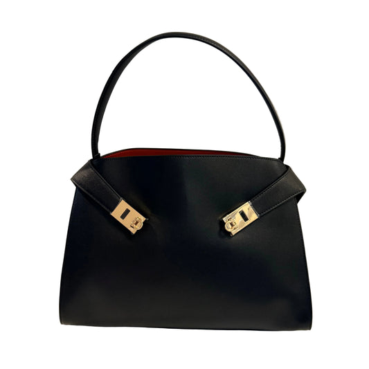 Black handbag with gold hardware on a light gray background