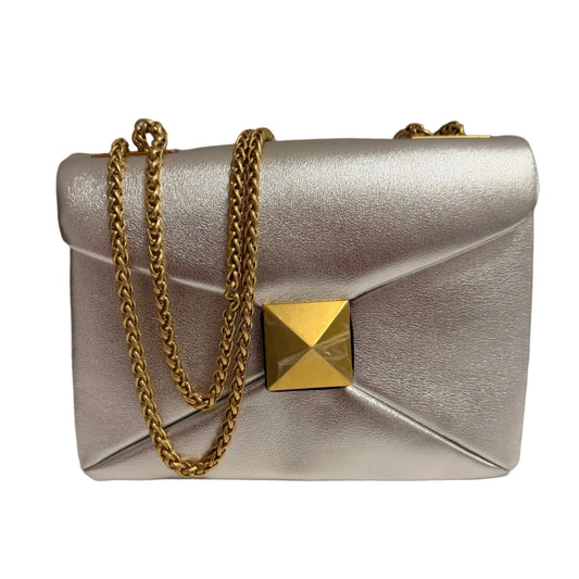 Silver handbag with a gold chain and clasp on a neutral background