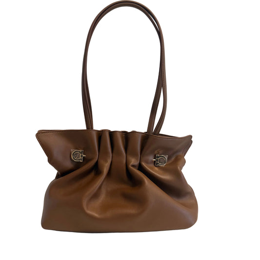 A brown leather shoulder bag with a gathered, slouchy silhouette, dual top handles, and silver-tone hardware on a plain light gray background.