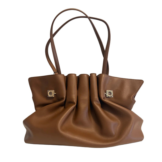 A brown leather handbag with gathered pleats and two shoulder straps, featuring silver-tone decorative hardware on the front, set against a plain light gray background.