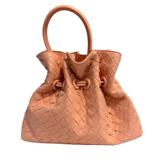 A light peach-pink woven leather handbag with a single top handle, resting on a white surface against a neutral gray background.