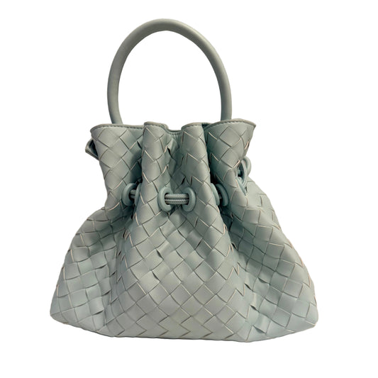 A light blue woven leather bucket bag with a single top handle, set against a plain beige background.