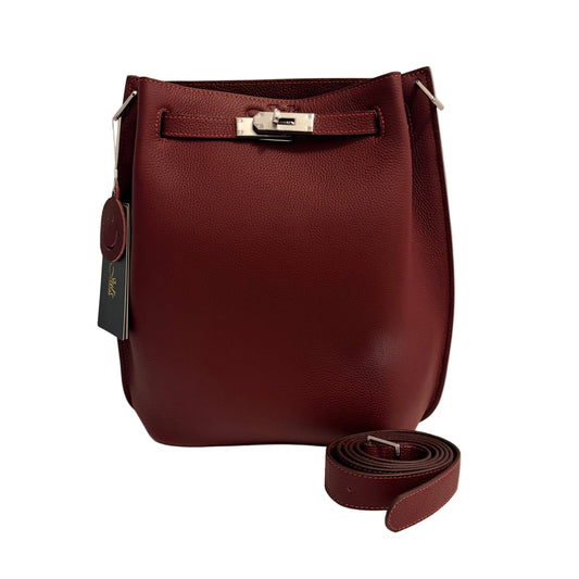 A burgundy pebbled leather bucket bag with silver-tone hardware, shown with its matching leather strap coiled in front on a white surface against a light gray background.