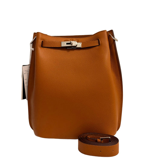 A tan pebbled leather bucket bag with silver-tone hardware, shown with its matching leather strap coiled in front on a white surface against a light gray background.