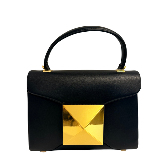 A structured black leather handbag with a top handle and a large metallic gold pyramid-shaped clasp on the front, shown against a plain white background.